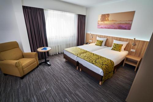ヒルフェルスムにあるアマラス ホテル レイパーシェーク アレーナパークのベッドと椅子付きのホテルルーム