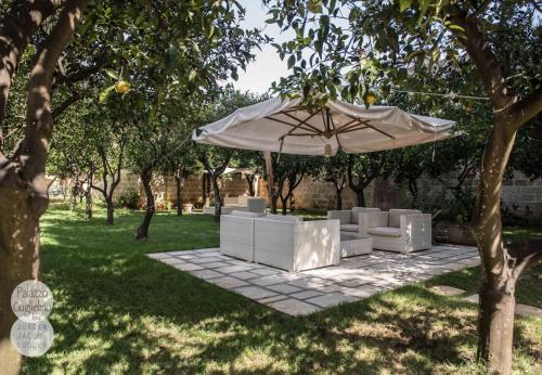 a patio with an umbrella and white chairs and trees at Palazzo Guglielmo in Vignacastrisi