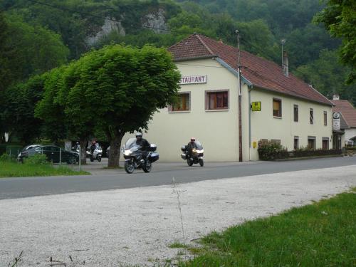 two people riding motorcycles down a road next to a building at L'auberge Des 3 Ponts in Cusance