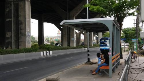 a woman and a child sitting at a bus stop at Natcha Place Rangsit Donmuang in Ban Talat Rangsit