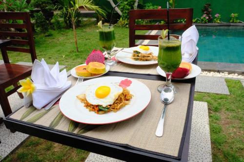 ein Tisch mit Tellern mit Frühstücksspeisen und Getränken in der Unterkunft Kubu Green in Nusa Dua