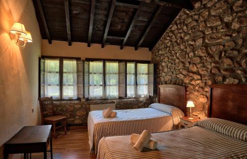 a bedroom with two beds and a stone wall at Complejo Rural La Tahona De Besnes in Alles