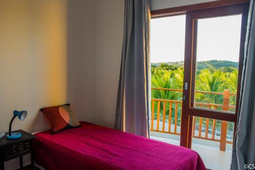 a bedroom with a red bed and a large window at Atlantica Apartamentos Imbassai in Imbassai