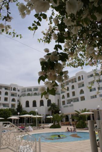 a large building with a swimming pool with white flowers at El Mouradi Hammamet in Hammamet