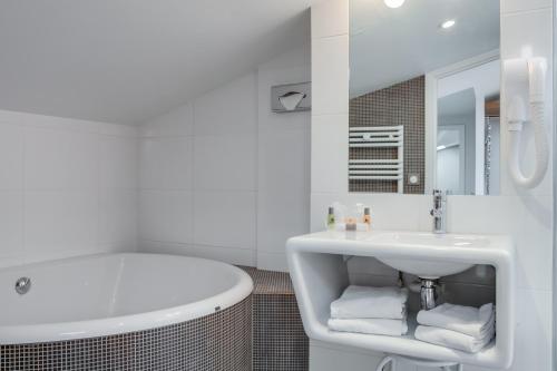 a white bathroom with a tub and a sink at The Originals Boutique, Hôtel Victoria, Fontainebleau in Fontainebleau