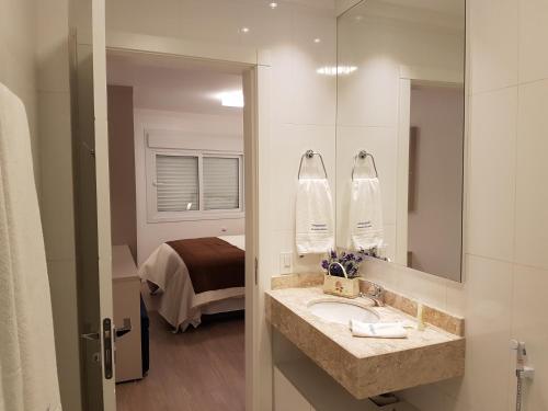baño con lavabo, espejo y cama en Temporada Gramado e Canela - Apartamento Centro Campos de Canella, en Canela
