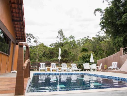 a swimming pool with white chairs and a table at Pousada Recanto da Serra in São Pedro da Serra
