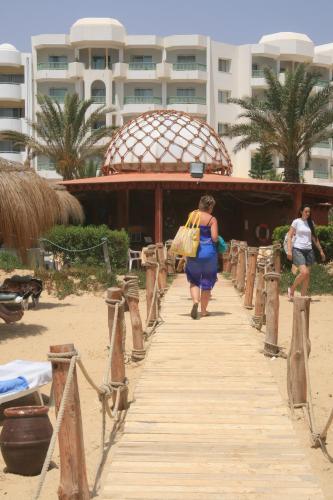 a woman walking down a wooden walkway on the beach at El Mouradi Hammamet in Hammamet
