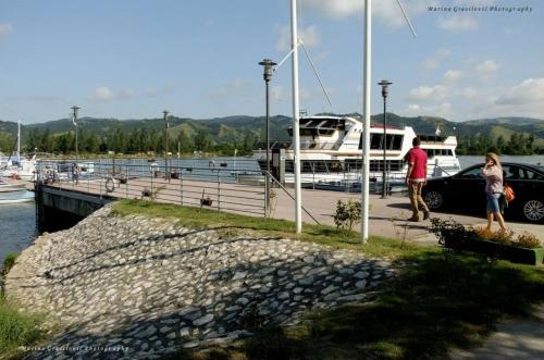 a man and woman standing near a marina with a boat at ATOS Srebrno jezero - Villa and Restaurant in Veliko Gradište