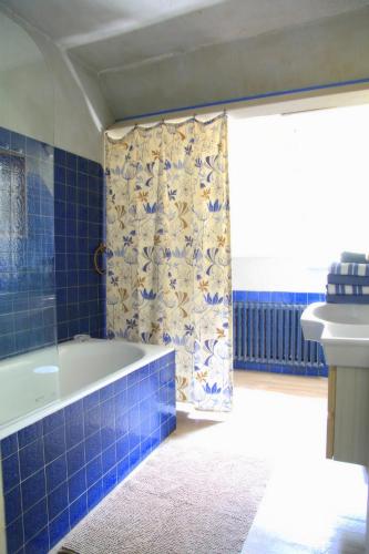 La salle de bains est pourvue de carrelage bleu, d'une baignoire et d'un lavabo. dans l'établissement Le moulin de Beuzidou, à Saint-Urbain
