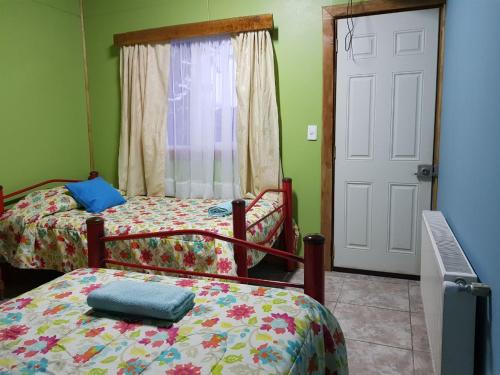 a bedroom with two beds and a window and a door at Hostal Aventura Austral in Punta Arenas