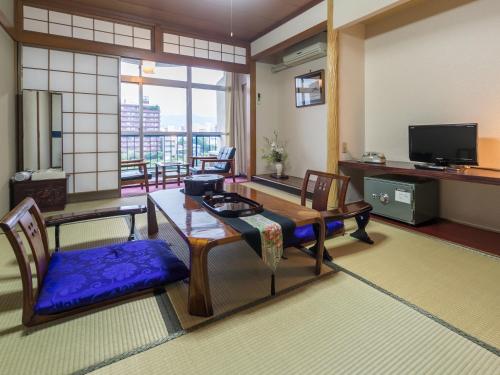 een woonkamer met een tafel en stoelen en een televisie bij Riverside Hotel Shoei in Kochi