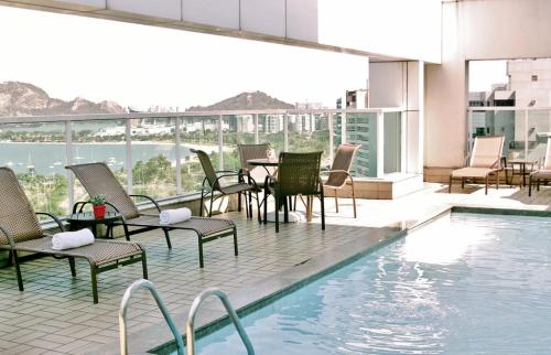 einem Pool mit Stühlen und einem Tisch auf einem Gebäude in der Unterkunft Praia do Canto Apart Hotel in Vitória