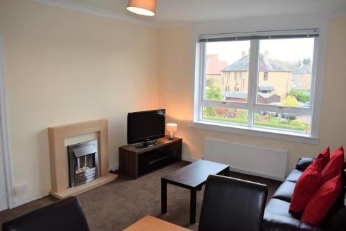 een woonkamer met een bank, een tv en een open haard bij Kelpies Serviced Apartments MacGregor- 2 Bedrooms in Grangemouth