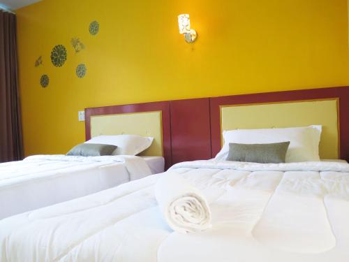 two beds in a room with a yellow wall at Your Place Inn Surin in Surin