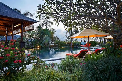 a swimming pool with tables and umbrellas and flowers at Villa L'Orange Bali in Keramas