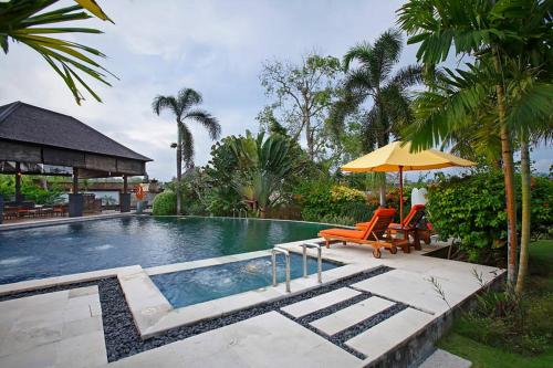 a swimming pool with two chairs and an umbrella at Villa L'Orange Bali in Keramas