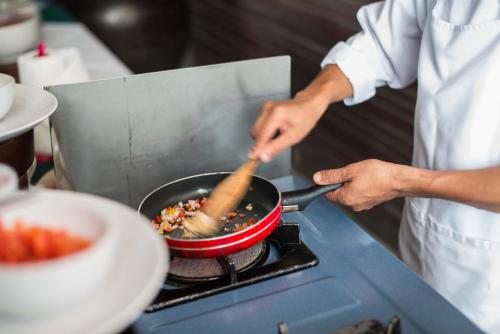 a person cooking food in a pan on a stove at The Hive Hotel - SHA Plus in Lamai