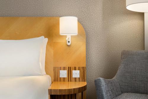 a bedroom with a bed and a chair and a lamp at Ramada Hotel & Suites by Wyndham Coventry in Coventry