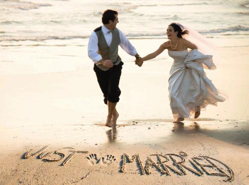 a bride and groom walking on the beach with the word vacation written in the sand at Grand Hotel Swanage in Swanage