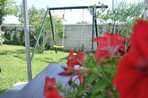 a table with red flowers and a swing at Apartments Smilja in Ljubač