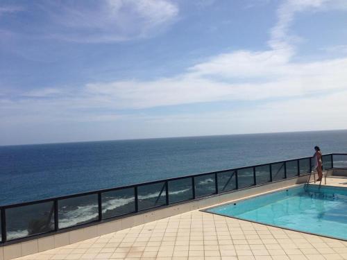 a person standing next to a swimming pool overlooking the ocean at Farol Barra Flat completo e bem localizado in Salvador