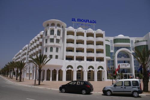 a white building with two cars parked in front of it at El Mouradi El Menzah in Hammamet
