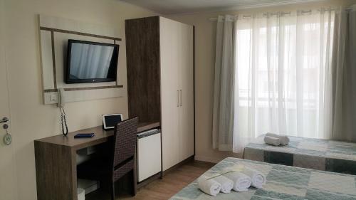 - une chambre avec un bureau, un lit et une télévision dans l'établissement Pousada Bomar Bombinhas, à Bombinhas