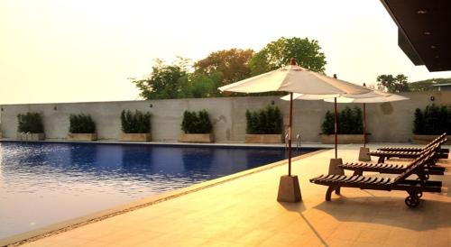 an umbrella and two benches next to a swimming pool at Green Hill Hotel Phayao in Phayao