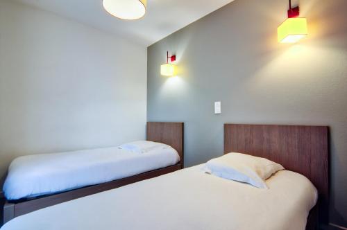 a bedroom with two beds and two lights on the wall at Zenitude Hôtel-Résidences Narbonne Centre in Narbonne