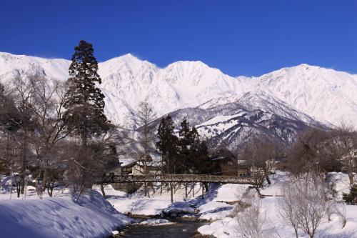 a snow covered mountain range with a bridge and trees at Hotel Hakuba in Hakuba