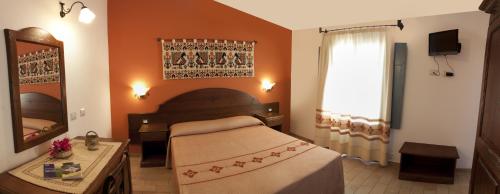 Schlafzimmer mit einem Bett, einem Spiegel und einem Fenster in der Unterkunft Hotel Bia Maore in Baunei