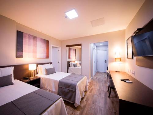 a hotel room with two beds and a flat screen tv at Vila Business Hotel in Volta Redonda