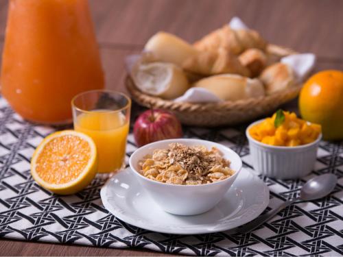 a table with a bowl of cereal and fruit and orange juice at Vila Business Hotel in Volta Redonda