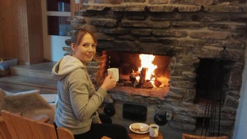 a woman holding a cup of coffee in front of a fireplace at Kuerkievari KuerHotel in Äkäslompolo
