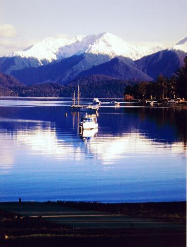 a boat is docked on a lake with snow covered mountains at Anchorage Motel Apartments in Te Anau