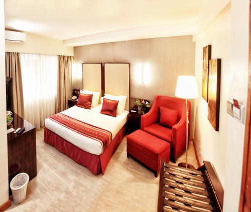 um quarto de hotel com uma cama e uma cadeira vermelha em The Zehneria By Sarovar Portico India em Nairobi