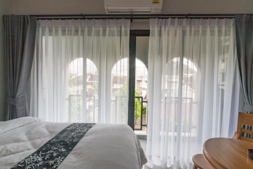 a bedroom with white curtains and a bed and a table at The Besavana Phuket - SHA Extra Plus in Phuket Town