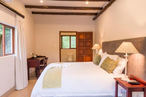 a bedroom with a large white bed and a desk at Hluhluwe Lodge by ANEW in Hluhluwe