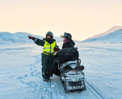 two people are standing in the snow with a snowmobile at Coal Miners’ Cabins in Longyearbyen