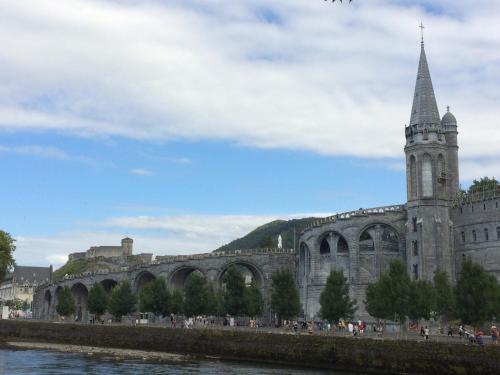 a large building with a clock tower and a river at Hôtel Majestic in Lourdes