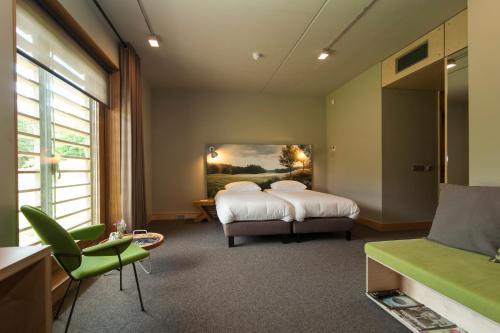 a bedroom with a bed and a green chair at Golf Lodge in Zeijerveen