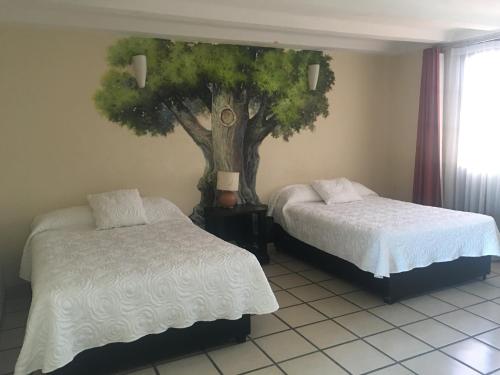 a bedroom with two beds and a tree on the wall at Hotel Calli Quetzalcoatl in Cholula