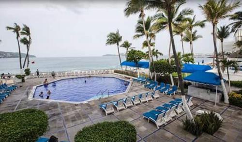 a swimming pool with blue chairs and the ocean at Hotel Acapulco Malibu in Acapulco