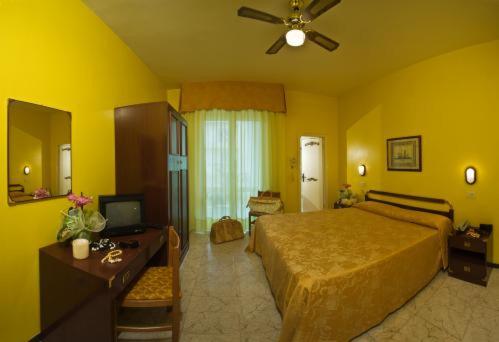 een gele slaapkamer met een bed, een bureau en een televisie bij Hotel Maremonti in Gabicce Mare