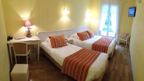 a hotel room with two beds and a desk and window at Auberge les Oliviers in Lucciana