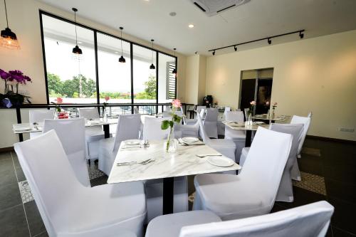 un restaurante con sillas blancas, mesas y ventanas en RHR Hotel - Selayang en Batu Caves