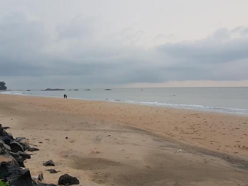 a beach with people walking on the sand and the ocean at White Shell Beach House in Kannur