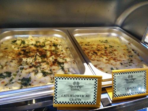 two trays of casserole dishes of food on a counter at Hype Motorsport Hotel Nilai in Nilai