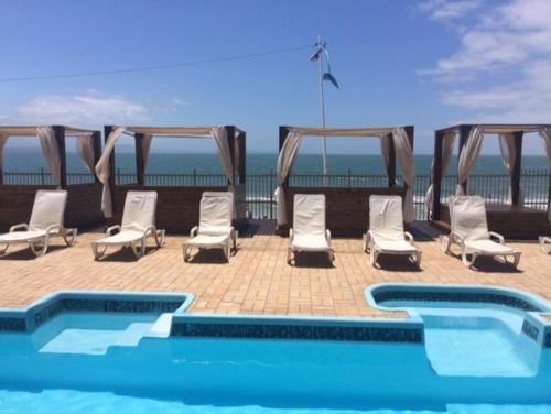 a swimming pool with chairs and a tent and the ocean at Canasvieiras Hotel in Florianópolis